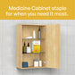 A light wood medicine cabinet with two doors open, showing shelves with toiletries and a box of OTC medicine, set against a tiled wall. A yellow banner at the top reads 'Medicine Cabinet staple for when you need it most.